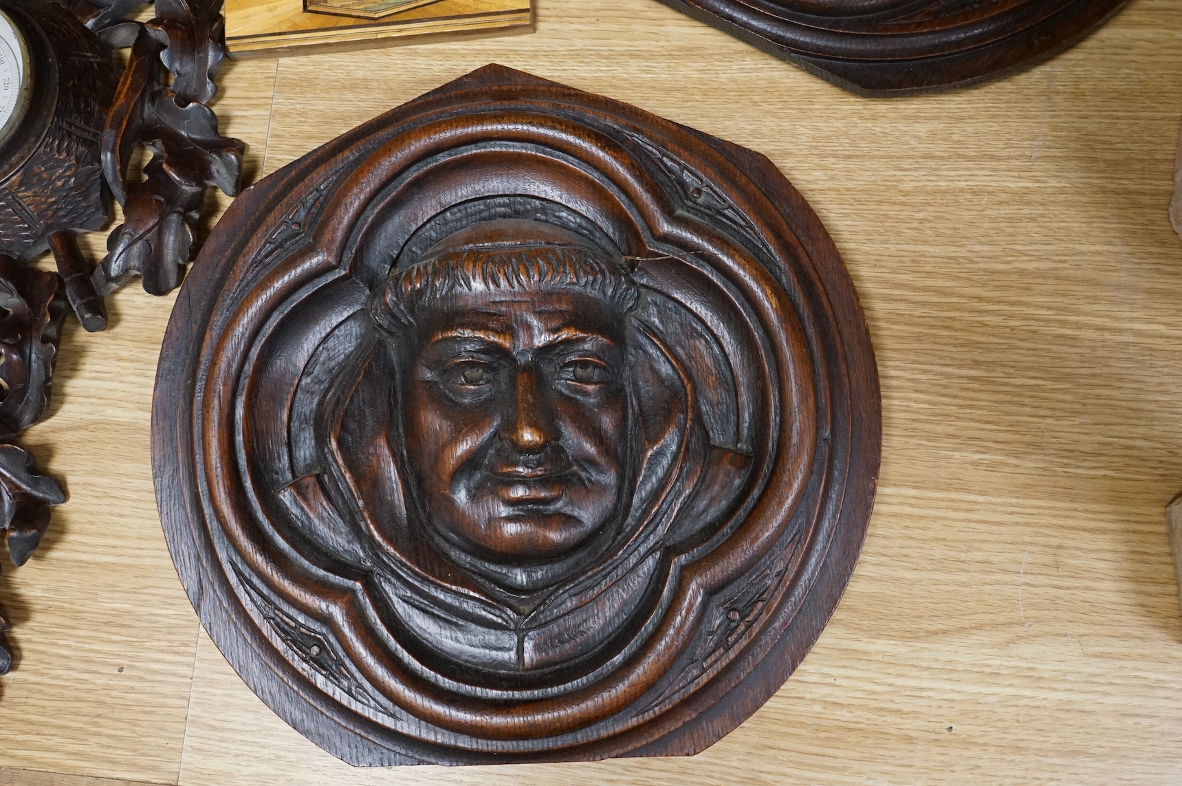 A pair of Gothic revival oak wall plaques, a Black Forest carved barometer, a Virgin and child figure, an IHS embroidered panel, two straw worked panels and a carved finial, barometer 47cm high